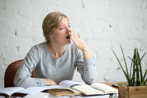 Ritratto di una studentessa sbadigliata alla scrivania