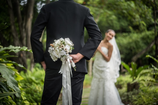 Ritratto di uno sposo che nasconde un bouquet di fiori dietro la schiena per la sorpresa di una sposa.