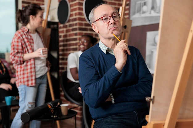 Ritratto di uno studente anziano che disegna un vaso su tela bianca che disegna il modello utilizzando la matita grafica in studio di creatività. Corso d'arte attento a un team eterogeneo che sviluppa nuove abilità artistiche per la crescita personale