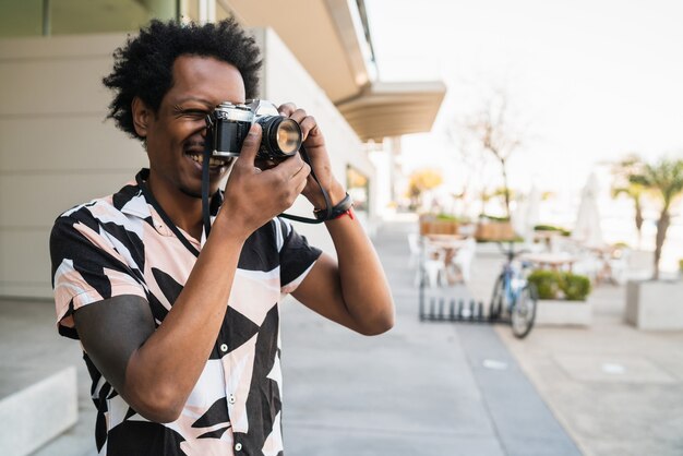 Ritratto di uomo afro che scatta fotografie con la fotocamera mentre si cammina all'aperto per strada