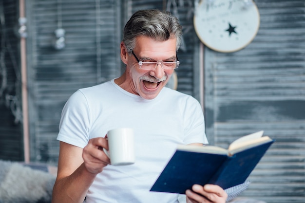 Ritratto di uomo anziano seduto sul letto, con in mano un libro, sorridente felicemente