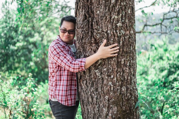 Ritratto di uomo asiatico felice che abbraccia un albero nella foresta Proteggere e amare la natura Concetto di ambiente ed ecologia