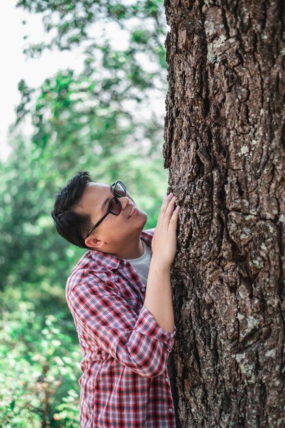 Ritratto di uomo asiatico felice che abbraccia un albero nella foresta Proteggere e amare la natura Concetto di ambiente ed ecologia