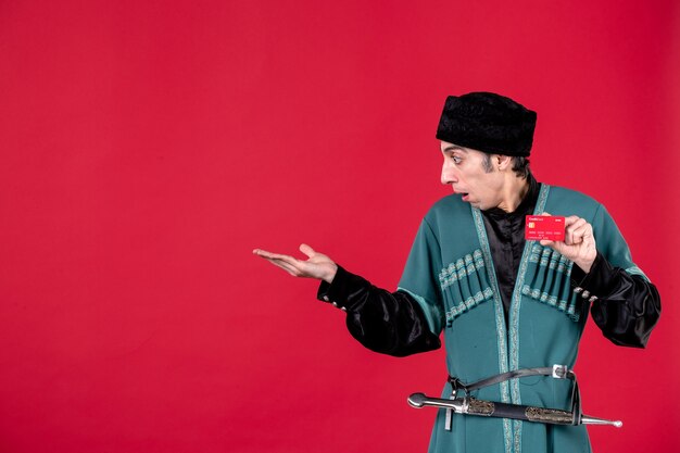 Ritratto di uomo azero in costume tradizionale in possesso di carta di credito su colore rosso primavera denaro etnico novruz