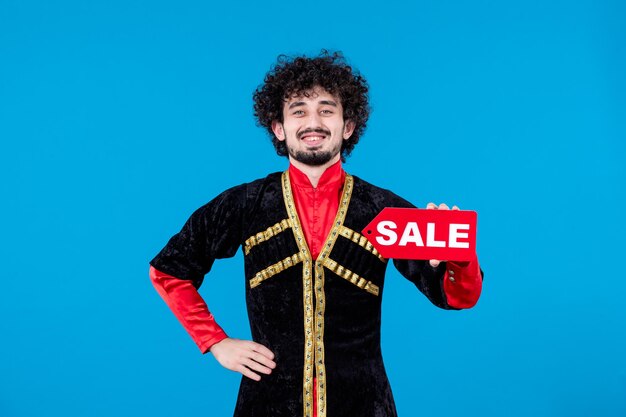 Ritratto di uomo azero sorridente in costume tradizionale che tiene targhetta di vendita su sfondo blu shopping etnico novruz