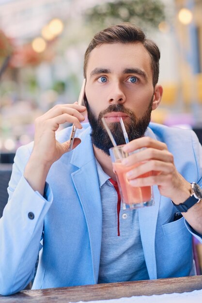 Ritratto di uomo barbuto alla moda in una giacca blu parla di smartphone.