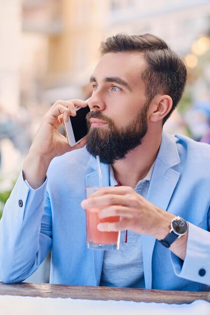 Ritratto di uomo barbuto alla moda in una giacca blu parla di smartphone.