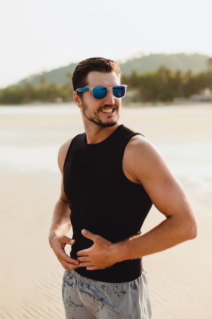 Ritratto di uomo bello all'aperto, in spiaggia. Indossare maglietta e pantaloncini neri senza maniche. Tempo caldo sole vicino al mare