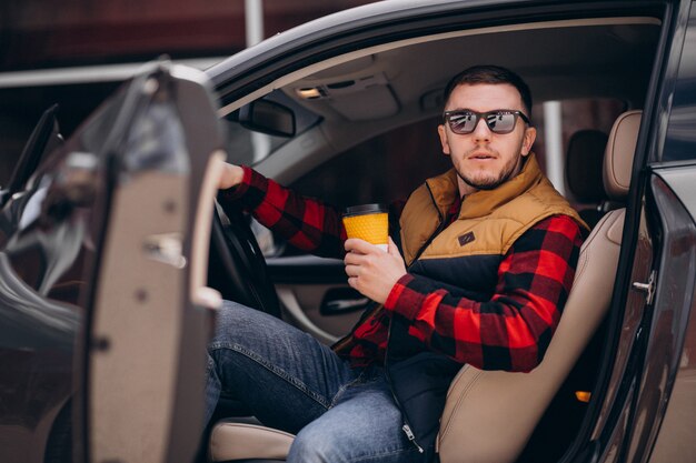 Ritratto di uomo bello seduto in macchina e bere caffè