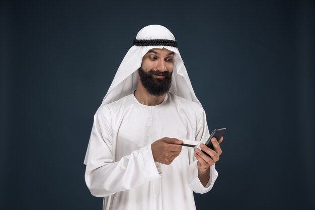 Ritratto di uomo d'affari arabo saudita. Uomo che utilizza smartphone per pagare la bolletta, acquisti online o scommesse. Concetto di affari, finanza, espressione facciale, emozioni umane.