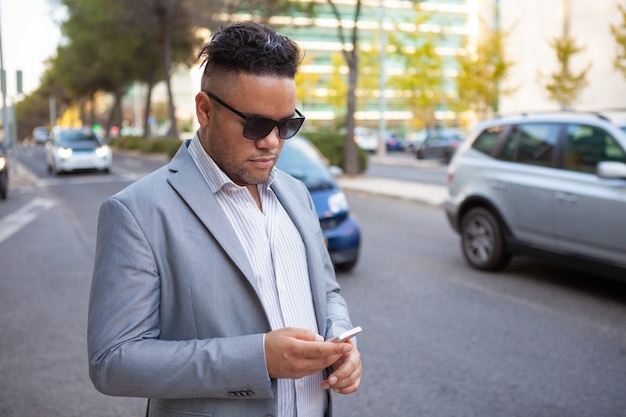 Ritratto di uomo d&#39;affari fiducioso in occhiali da sole con smartphone