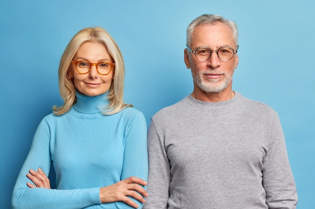 Ritratto di uomo e donna matura stare uno accanto all'altro in abiti casual contro il muro blu guarda direttamente davanti con espressioni calme