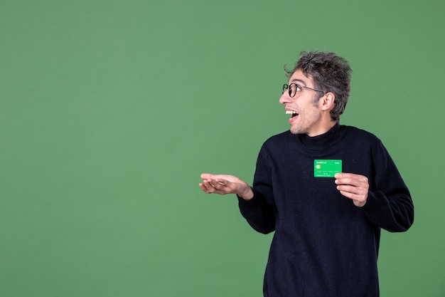 Ritratto di uomo genio in possesso di carta di credito in studio shot parete verde