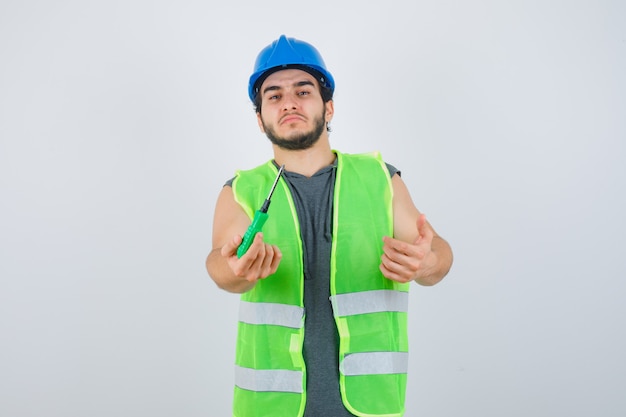 Ritratto di uomo giovane costruttore allungando la mano per dare un cacciavite in uniforme e guardando fiducioso vista frontale