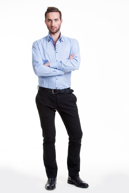 Ritratto di uomo serio in camicia blu e pantaloni neri con le braccia incrociate - isolato su bianco