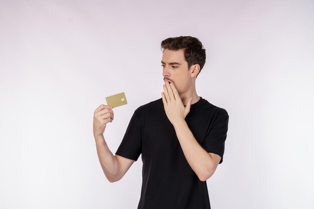 Ritratto di uomo sorpreso in abiti casual che mostra la carta di credito isolata su sfondo bianco