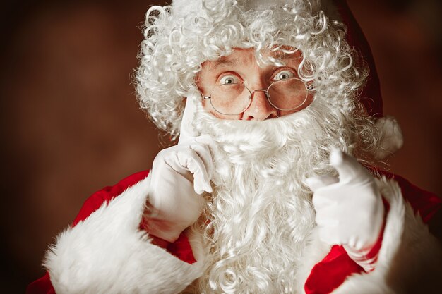 Ritratto di uomo sorpreso in costume di Babbo Natale con una lussuosa barba bianca, cappello di Babbo Natale e un costume rosso in rosso