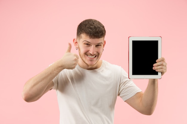 Ritratto di uomo sorridente che punta al computer portatile con schermo vuoto isolato su sfondo rosa studio. e concetto di pubblicità.