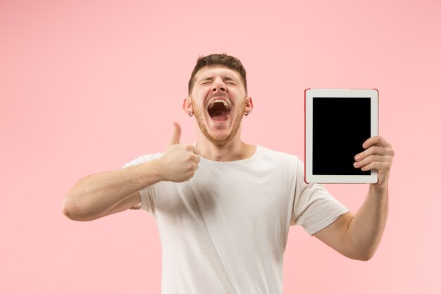 Ritratto di uomo sorridente che punta al computer portatile con schermo vuoto isolato su sfondo rosa studio. Emozioni umane, concetto di espressione facciale e concetto di pubblicità.