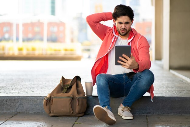 Ritratto di uomo stressato e preoccupato utilizzando la tavoletta digitale mentre è seduto all'aperto. Concetto urbano.