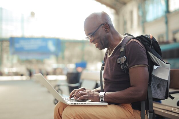 ritratto di uomo su una panchina nella stazione ferroviaria mentre si utilizza un computer
