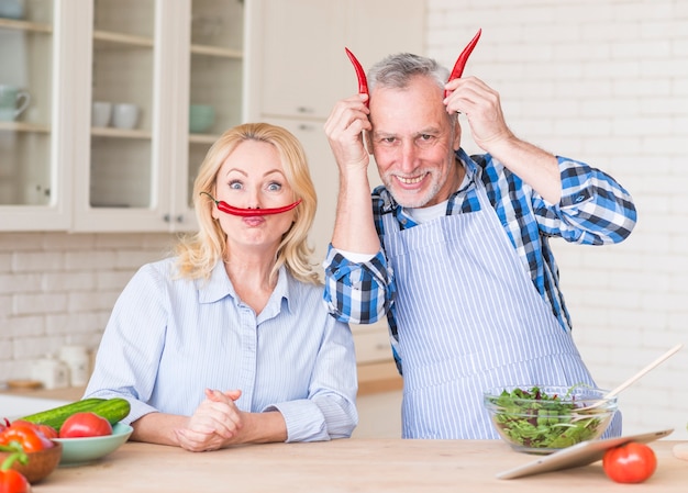 Ritratto divertente di una coppia senior con i peperoncini rossi nella cucina