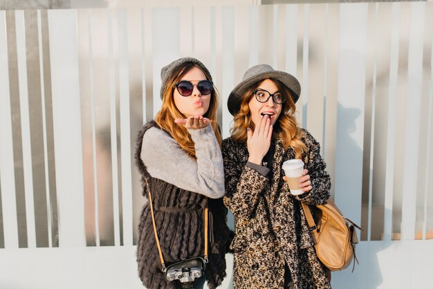 Ritratto due donne felici divertenti alla moda divertendosi sulla strada in città. Giornata di sole di giovane donna alla moda che viaggiano insieme, esprimendo positività, emozioni vere, giocoso, godendosi il sole, sorridendo.