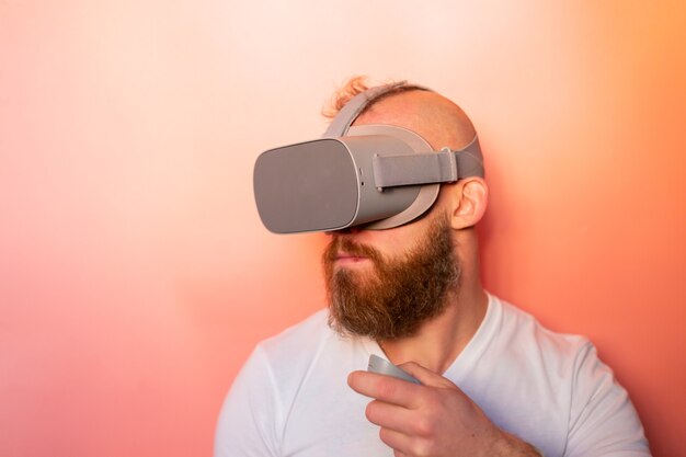 Ritratto emotivo di un uomo con la barba che indossa occhiali per realtà virtuale in studio su uno sfondo rosa arancio