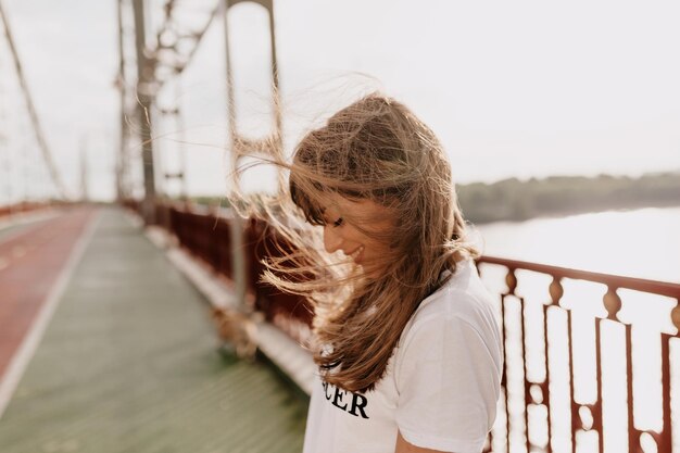 Ritratto esterno di una ragazza attraente che sorride con meravigliose emozioni felici e copre il viso con i capelli volanti