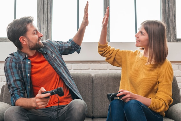 Ritratto felice di una giovane coppia che si siede sul divano dando il cinque a vicenda mentre si gioca video gioco