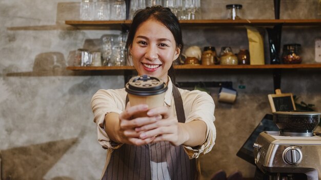 Ritratto giovane signora asiatica barista cameriera tenendo tazza di caffè sentirsi felice al caffè urbano.