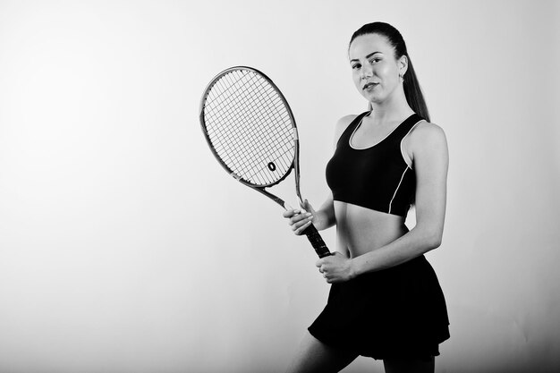 Ritratto in bianco e nero di una bella giovane donna in abiti sportivi che tiene una racchetta da tennis mentre si trova su uno sfondo bianco