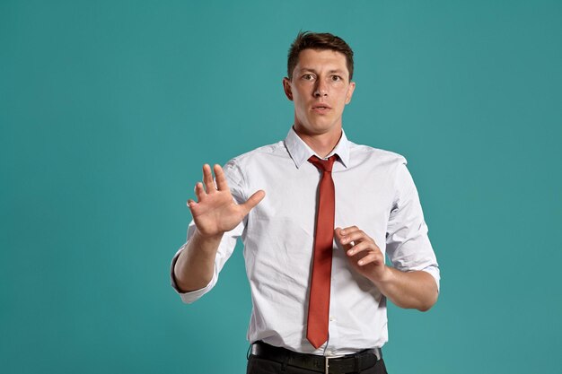 Ritratto in studio di un giovane uomo d'affari maestoso in una classica camicia bianca e cravatta rossa che sembra confuso mentre posa su uno sfondo blu. Taglio di capelli alla moda. Concetto di emozioni sincere. Copia spazio.