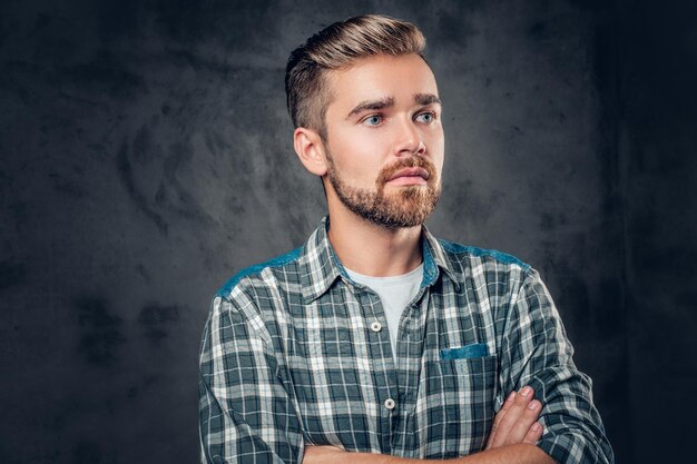 Ritratto in studio di un maschio hipster con la barba e gli occhi azzurri con le braccia incrociate su sfondo grigio.