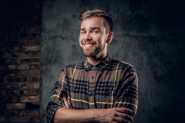 Ritratto in studio di un maschio hipster con la barba e gli occhi azzurri con le braccia incrociate su sfondo grigio.