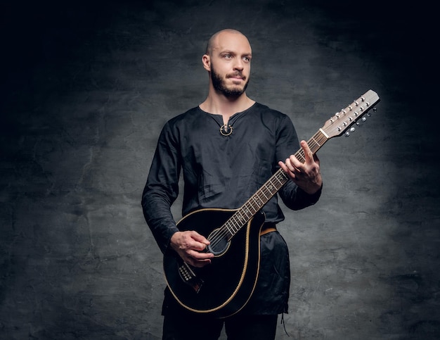 Ritratto in studio di un uomo nei tradizionali abiti celtici che gioca sul mandolino su sfondo grigio vignetta.