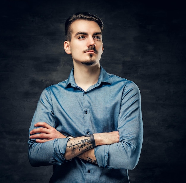 Ritratto in studio di uomo alla moda con le braccia incrociate, vestito con una camicia blu su sfondo grigio.