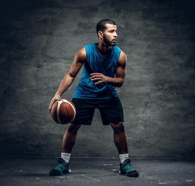 Ritratto in studio per tutto il corpo di un giocatore di basket nero che gioca con una palla.