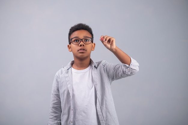 Ritratto in vita di un ragazzo concentrato con una camicia a righe e occhiali che fa uno schizzo