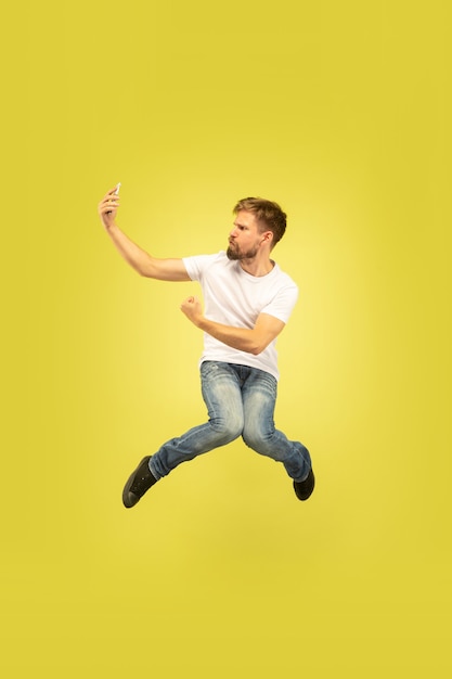 Ritratto integrale dell'uomo di salto felice isolato su priorità bassa gialla. Modello maschio caucasico in abiti casual. Libertà di scelte, ispirazione, concetto di emozioni umane. Si fa selfie in fuga.