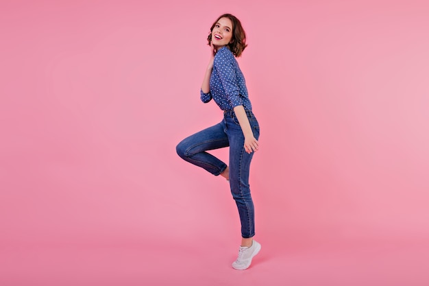 Ritratto integrale della ragazza sportiva con capelli ondulati. Tiro al coperto di saltare la giovane donna in jeans e maglietta blu.