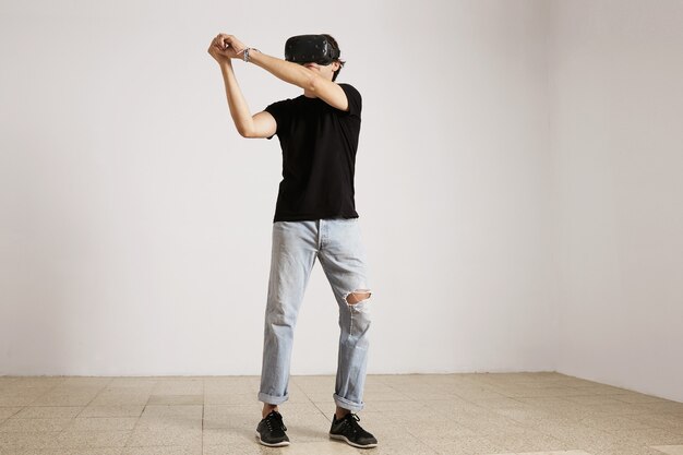 Ritratto integrale di un giovane modello caucasico in jeans strappati blu chiaro e maglietta nera che gioca baseball o tennis in vetri di Vr