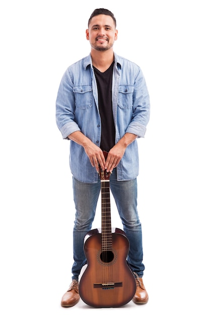 Ritratto integrale di un giovane uomo latino bello che tiene una chitarra classica su uno sfondo bianco