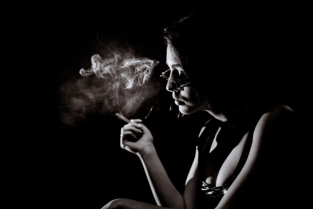 Ritratto monocromatico della ragazza che sta fumando con il grande decollete e in occhiali