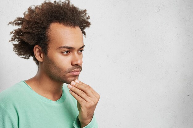 Ritratto orizzontale di pensieroso uomo di razza mista con acconciatura afro, tiene la mano sul mento