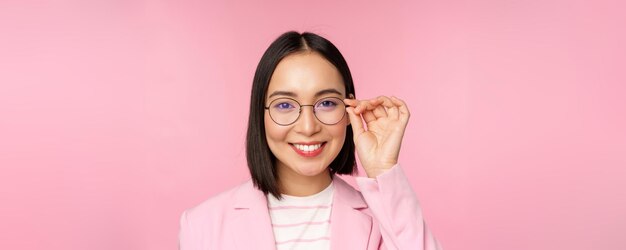 Ritratto ravvicinato di donna d'affari asiatica professionale imprenditrice in occhiali sorridente e guardando fiducioso sullo sfondo rosa della fotocamera