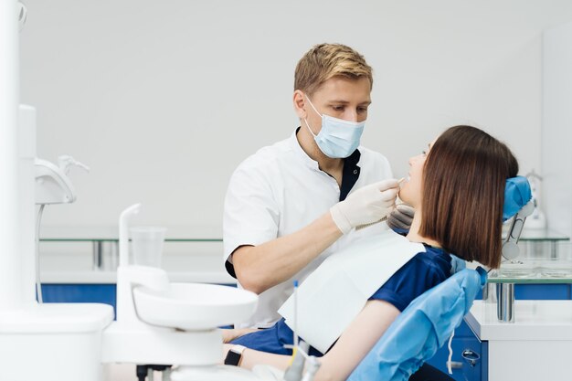 Ritratto ravvicinato di una bellissima giovane donna seduta su una poltrona odontoiatrica mentre lo stomatologo mani in guanti sterili che tengono campioni di denti