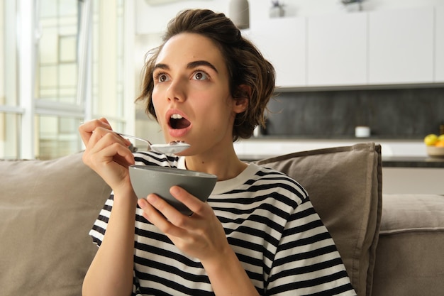 Ritratto ravvicinato di una donna che mangia davanti alla TV con l'aspetto stupito e con l'interesse a mangiare sullo schermo