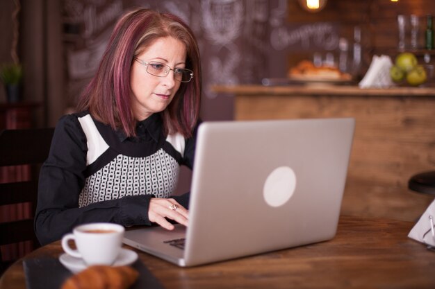 Ritratto ravvicinato di una donna d'affari adulta che lavora al computer portatile e si gode un caffè mattutino