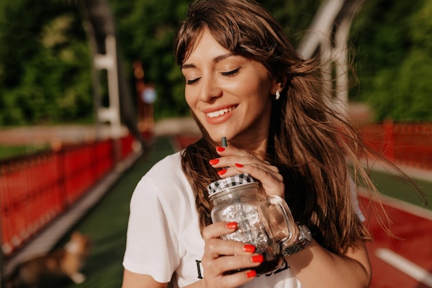 Ritratto ravvicinato di una ragazza affascinante con un sorriso ampio e meraviglioso che si gode il caffè del mattino con gli occhi chiusi alla luce del sole